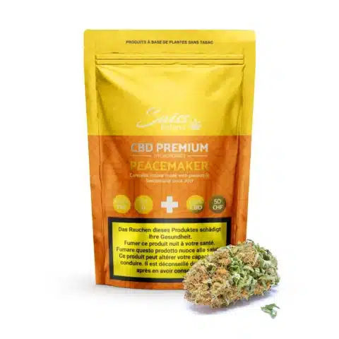 Un paquet jaune de swiss botanic fleurs de cbd indoor peacemaker - 0. 3% thc se tient debout avec une pile de bourgeons de cannabis séchés devant lui.