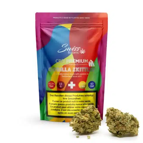 Un paquet coloré de swiss botanic fleurs de cbd indoor gorilla zkittlez - 0. 3% thc se tient debout, avec deux bourgeons de cannabis devant. Le texte indique la teneur en cbd/thc et les avertissements sanitaires en plusieurs langues.