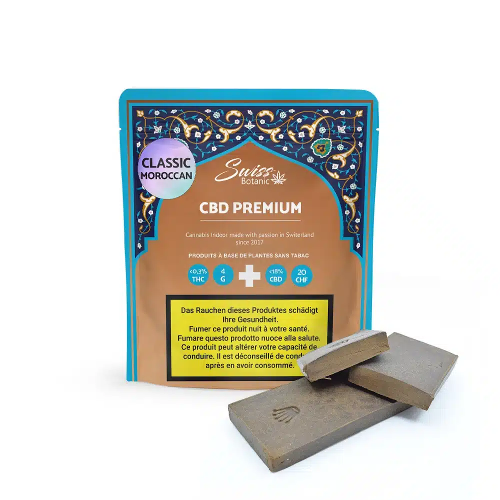 A packet labeled "Classic Moroccan Hash CBD Premium -" stands upright beside two pieces of brown, hash-like solid.