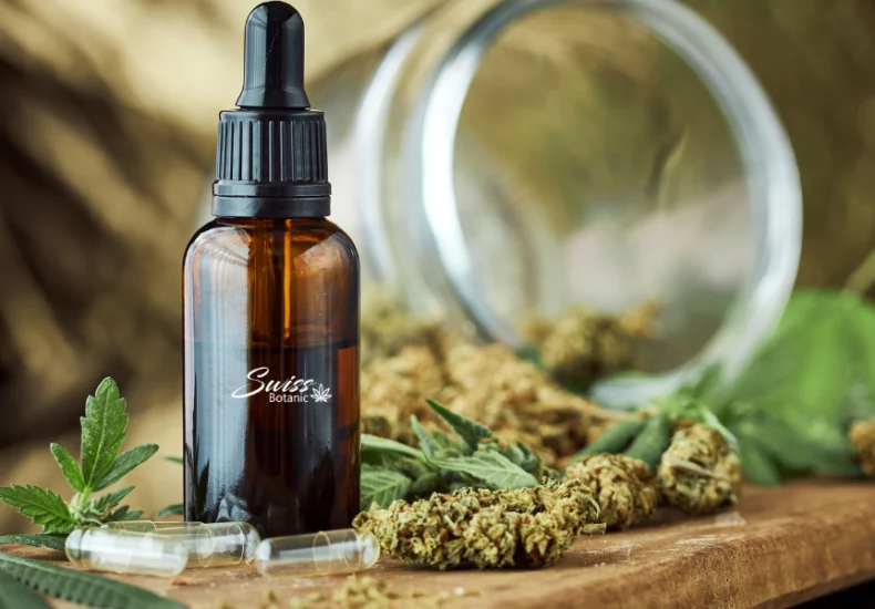 A bottle of cbd oil next to cannabis leaves.