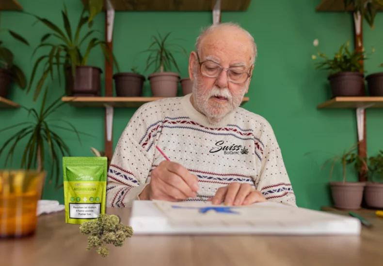 Un homme âgé avec des lunettes est assis à une table et se concentre sur l'écriture dans un cahier, avec un petit sac étiqueté « sativa » et des herbes dispersées visibles sur la table à côté d'un verre de liquide orange.