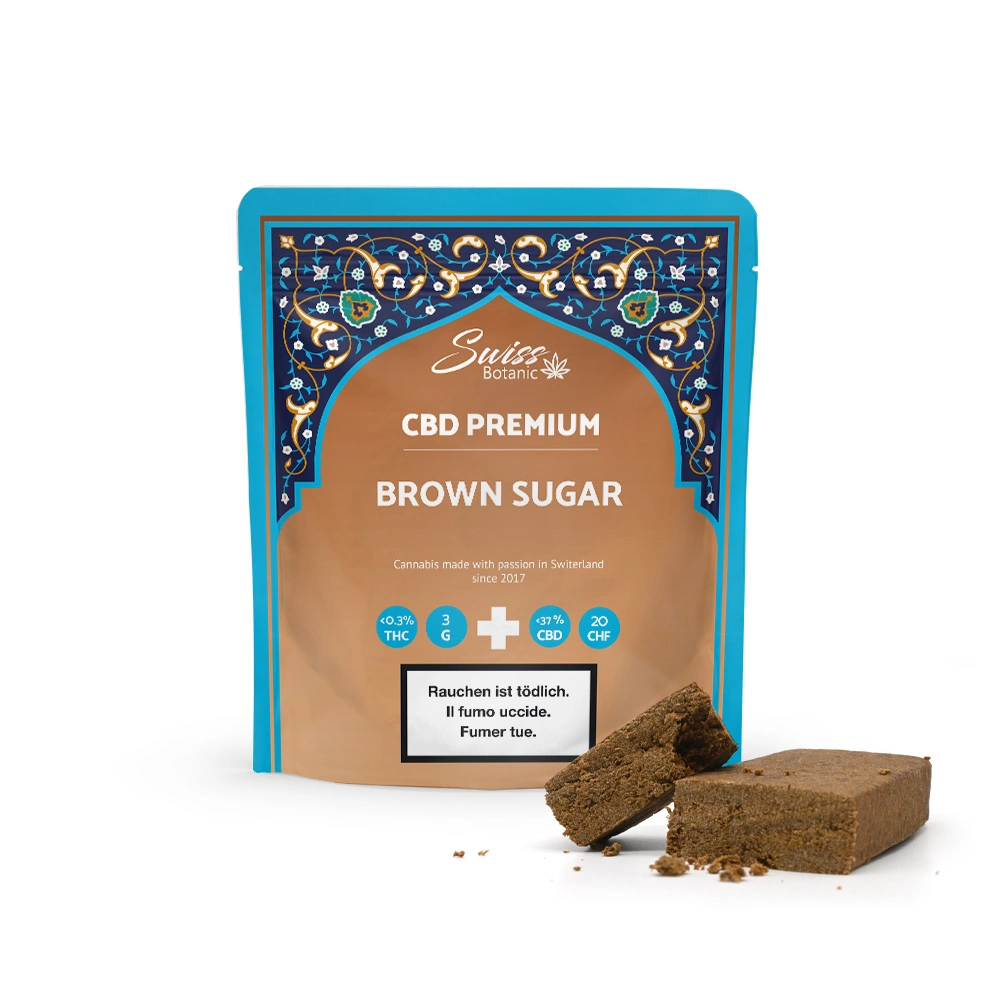 Paquete de azúcar moreno premium con CBD de Swiss Botanic con un diseño intrincado. Dos piezas de azúcar moreno expuestas fuera del paquete.